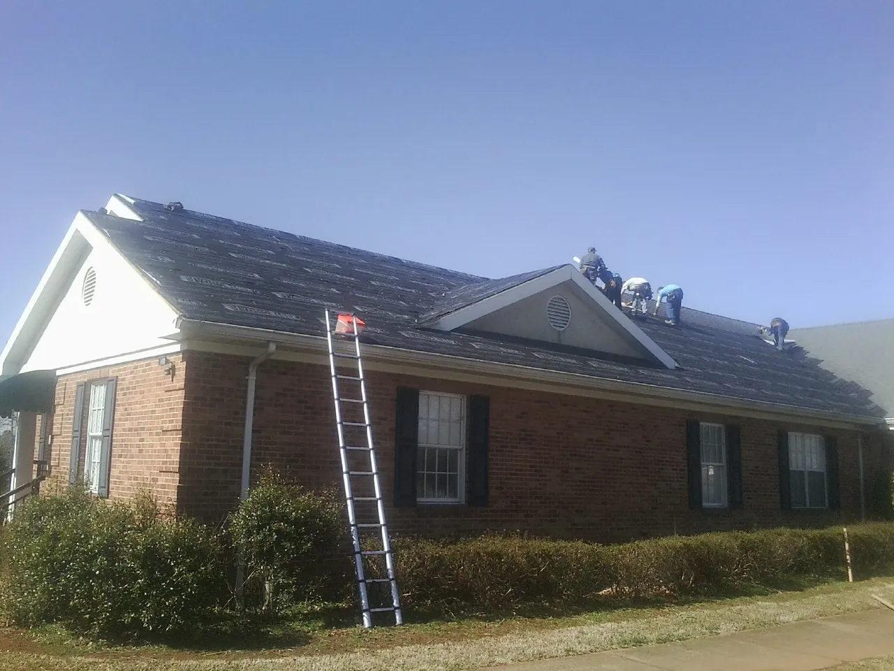 Crew tearing shingles off a brick ranch roof with a ladder set — Emergency Roof Repair work by our crew in Ormond Beach