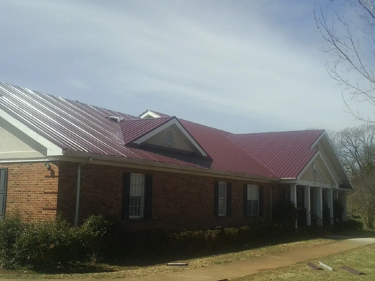 Red metal roof with gabled entries on a long brick building, from a Hail Damage Roof Repair job in Ormond Beach