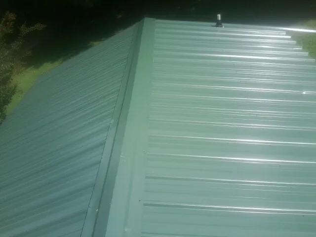 New green metal panels meeting at the ridge of a roof — Flat Roof Repair work by our crew in Ormond Beach