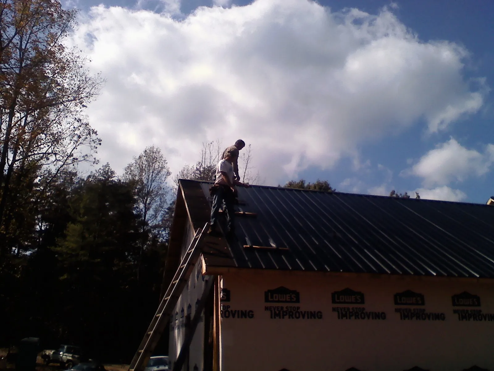Roofer fastening dark metal panels high against a cloudy sky, from a Roof Inspection job in Ormond Beach