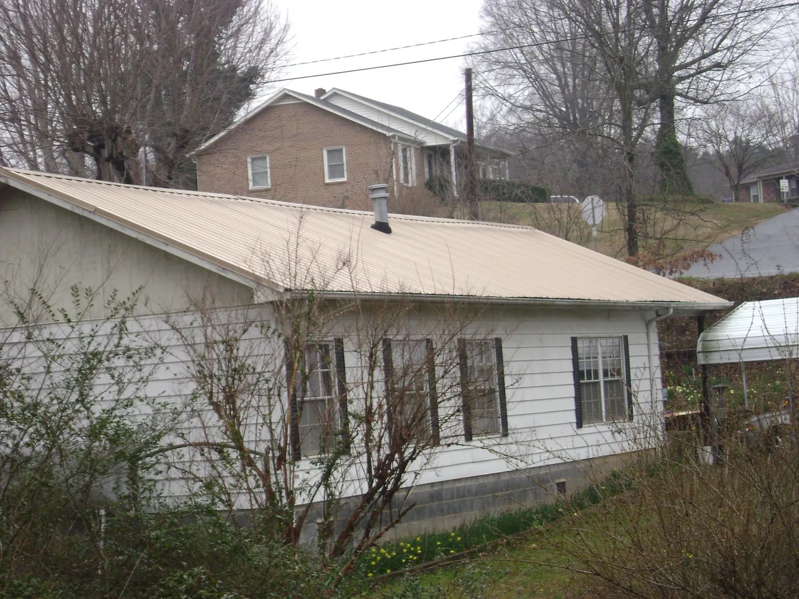 Tan metal roof on a white sided house set into a hillside — Commercial Roofing by Roofing Brothers in Ormond Beach