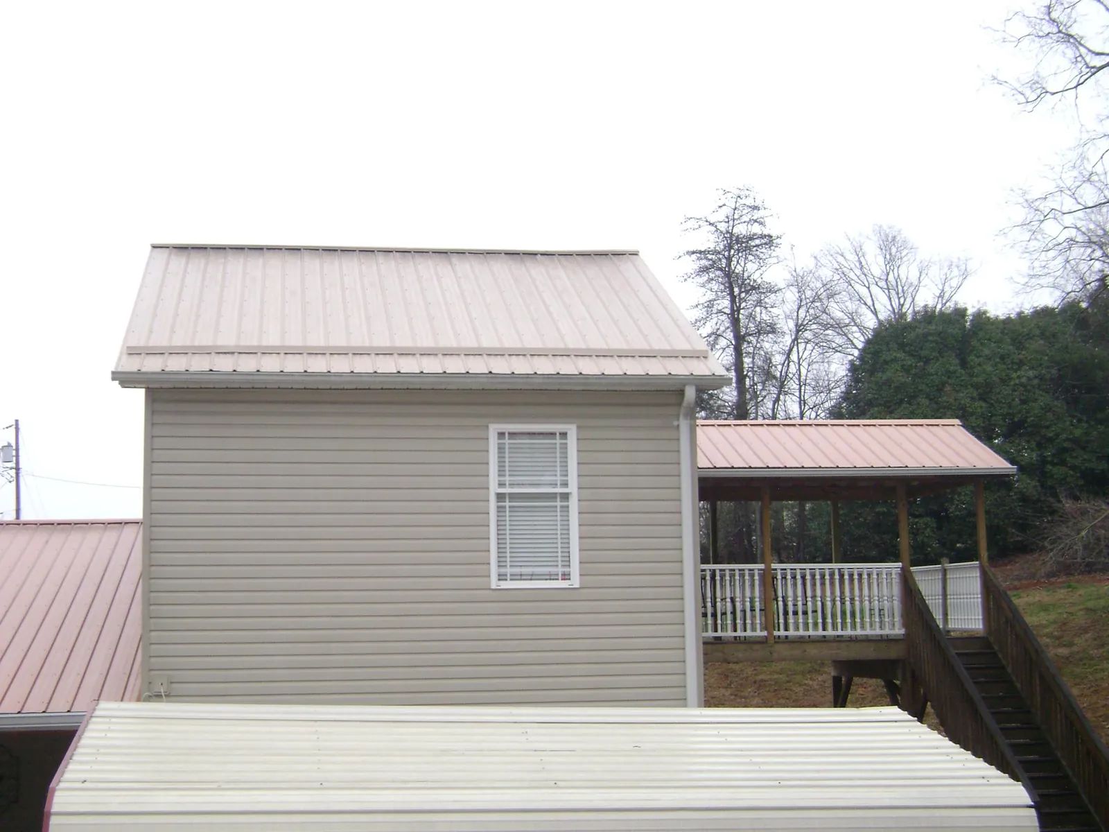 Tan metal roofs on a two story addition and attached porch, from a Roof Replacement job in Ormond Beach